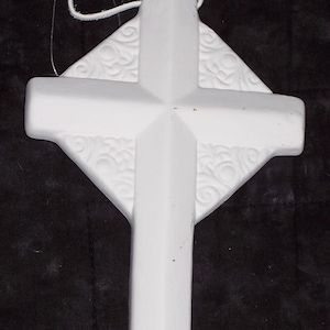 May include: A white ceramic cross-shaped ornament with a decorative embossed pattern on the arms. It has a cord for hanging. The cross is a religious symbol, often used for decoration.