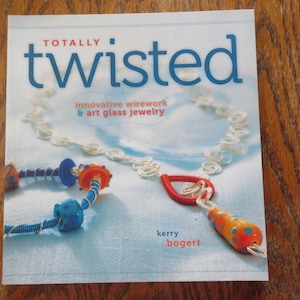 May include: A book cover titled "Totally Twisted" featuring innovative wirework and art glass jewelry. The cover displays a necklace and other jewelry pieces with blue, orange, and red accents. The author's name, Kerry Bogert, is also visible.