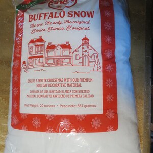 May include: A clear plastic bag filled with white Buffalo Snow. The bag has a red and white label with the text "BUFFALO SNOW" and "ENJOY A WHITE CHRISTMAS". The net weight is 20 ounces.
