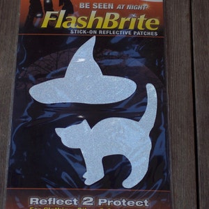 May include: A package of FlashBrite stick-on reflective patches featuring a silver witch hat and a cat silhouette. The packaging includes the text 3M Scotchlite Reflective Material, BE SEEN AT NIGHT, FlashBrite, and REFLECT 2 PROTECT For Clothing, Bikes & Accessories.
