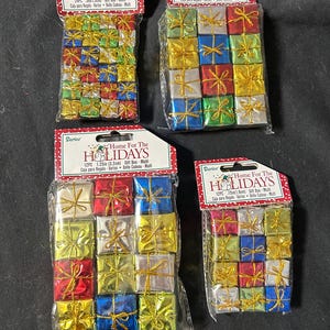 May include: Four packages of miniature gift boxes in various colors, including gold, red, blue, and silver, tied with gold or silver ribbons. Each package has a red and white label that reads "Home For The Holidays".