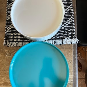 May include: Stack of white and turquoise round plates. The white plates are stacked on top of each other, and the turquoise plate is below. The plates are on a black and white patterned surface.