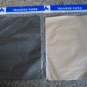May include: Two packages of Acclaim brand transfer paper in a clear plastic sleeve. One package contains dark charcoal sheets, and the other contains light tan sheets. Each blue header label features the text TRANSFER PAPER and the Acclaim logo.