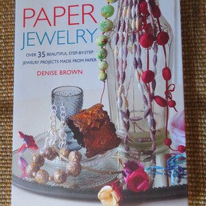 May include: A book titled "PAPER JEWELRY" with the subtitle "OVER 35 BEAUTIFUL STEP-BY-STEP JEWELRY PROJECTS MADE FROM PAPER" by Denise Brown. The cover features colorful paper jewelry and decorative items, including necklaces and a glass vase.