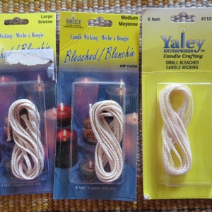 May include: Three packages of candle wicking. The packages are yellow and blue, with clear plastic windows displaying the wicking. The wicking is a cream color and is packaged in different lengths: 4 feet, 6 feet, and a smaller size.