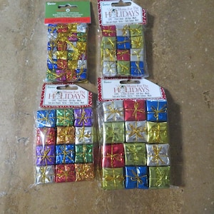 May include: Four packages of miniature gift box ornaments in various colors, including red, blue, green, and gold. Each box is wrapped with a gold ribbon. The packaging includes the text "Home For The Holidays."