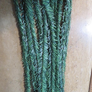 May include: Several strands of artificial evergreen garland, each composed of numerous small, dark green plastic needles. The garland is arranged in a vertical pattern, with the tips of the strands at the top and bottom.