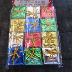 May include: A package of 12 small, colorful gift boxes, each approximately 1 inch (2.5 cm) square, wrapped in shiny foil. The boxes are in various colors, including green, gold, red, blue, and silver, and tied with gold ribbon. The packaging reads "Gift Box Multi".