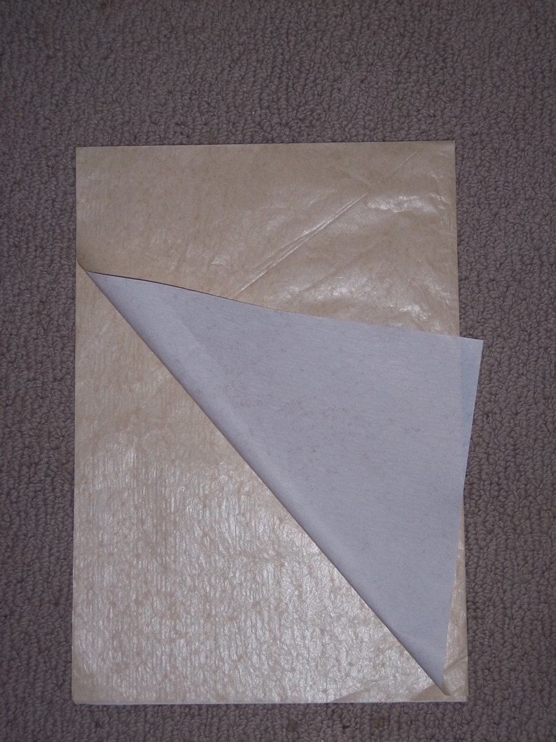 May include: A rectangular sheet of light tan, textured paper with a smooth, white, semi-transparent layer partially peeled back from the top left corner, revealing the contrasting textures and colors of the two distinct paper surfaces.