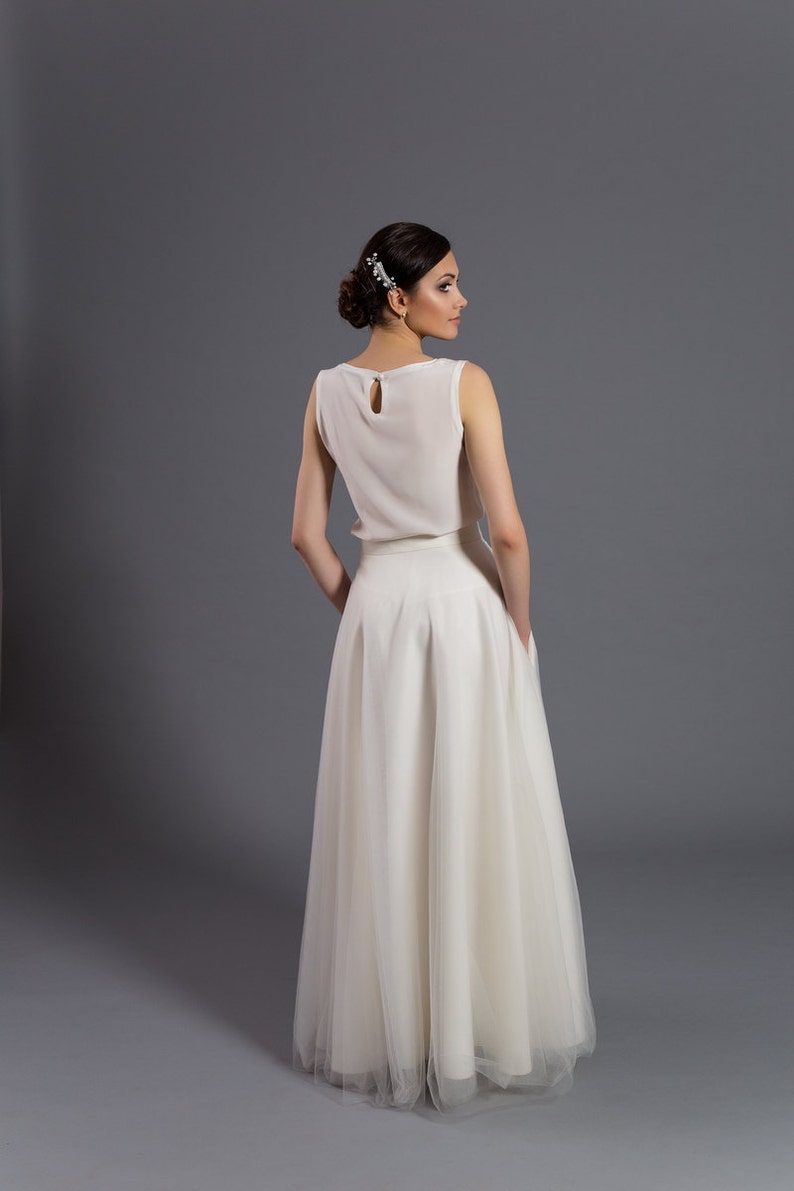 May include: A white sleeveless top with a keyhole back detail paired with a white tulle skirt. The skirt has a full, flowing silhouette.