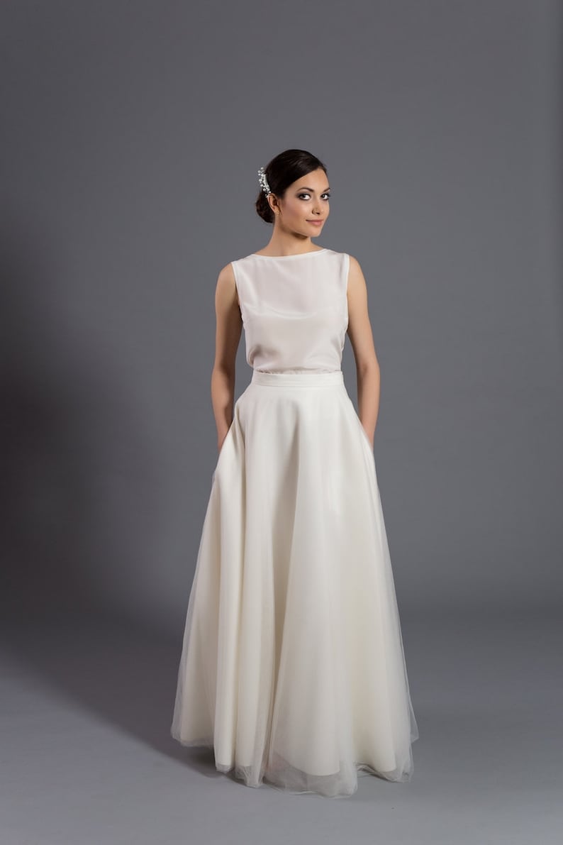May include: A white sleeveless top with a boat neck and a white tulle skirt. The skirt has a wide waistband and pockets on the sides.