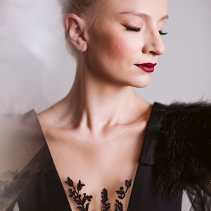 May include: A woman with blonde hair styled in a bun wears a black dress with a sheer lace bodice and a black fur stole. The dress features a floral design on the bodice.