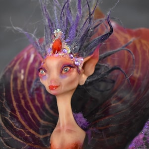May include: A purple and red fairy doll with a crown of rhinestones and a red gem. The fairy has long, purple hair and large, green eyes. The fairy is wearing a purple and red dress with a large, purple wing.