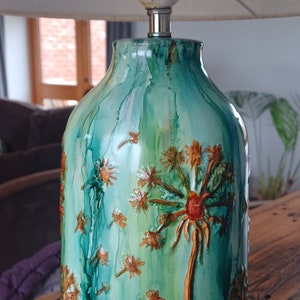 May include: A green and gold ceramic table lamp with a white linen shade. The lamp base features a hand-painted design of dandelions.