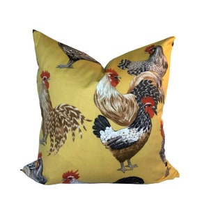 May include: A yellow throw pillow with a repeating pattern of roosters and hens. The pillow features a variety of colors, including brown, black, white, and red.