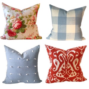 May include: Four decorative throw pillows with different patterns. The first pillow has a floral pattern with red, pink, and white flowers on a light blue background. The second pillow has a blue and white gingham pattern. The third pillow has a light blue background with white stitching and white tassels. The fourth pillow has a red background with a white ikat pattern.