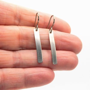 May include: A pair of silver bar earrings with a brushed finish. The earrings are simple and elegant, and they would make a great gift for any occasion.
