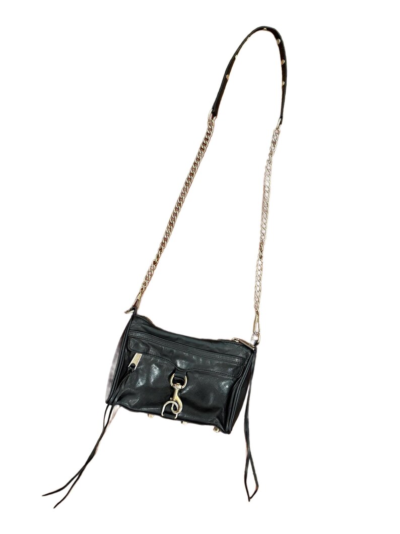 May include: A black leather crossbody bag featuring a silver-tone chain and leather strap, a front zippered pocket with a prominent silver lobster clasp closure, and two long leather zipper pulls hanging from the sides of the main compartment.