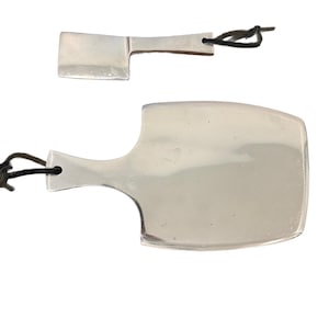 May include: Two polished silver-toned metal tools with flat, rectangular heads and short handles. Each tool features a small hole at the end of the handle, threaded with a thin, dark brown leather cord for hanging or storage purposes.