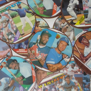 Puede incluir: Una colección de tarjetas de béisbol para coleccionar con varios jugadores, incluidos Mike Schmidt, Willie Mays y Rickey Henderson. Las tarjetas están dispuestas en forma circular y presentan una variedad de colores, incluidos rojo, blanco, azul y verde.