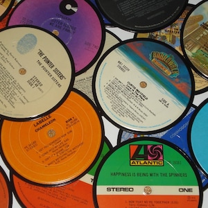 May include: A collection of vintage vinyl records with colorful labels. The records feature various artists and song titles, including "The Pointer Sisters" and "Happiness Is Being With The Spinners." The labels display text and logos.