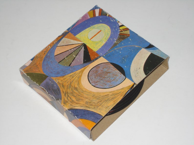 May include: A cardboard box with a colorful abstract design. The artwork features a mix of blue, orange, yellow, and purple shapes. The box is angled, showing the patterned top and the plain brown sides.