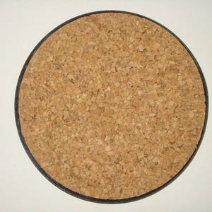 May include: Round cork coaster with a black border. The coaster is made of natural cork material, displaying a light brown, textured surface. This coaster is designed to protect surfaces from drink condensation.