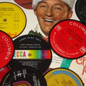 May include: A collection of vintage Christmas vinyl records, including albums by The Beach Boys, Barbra Streisand, and Bing Crosby. The records feature colorful labels with song titles and artist names, creating a festive holiday theme.