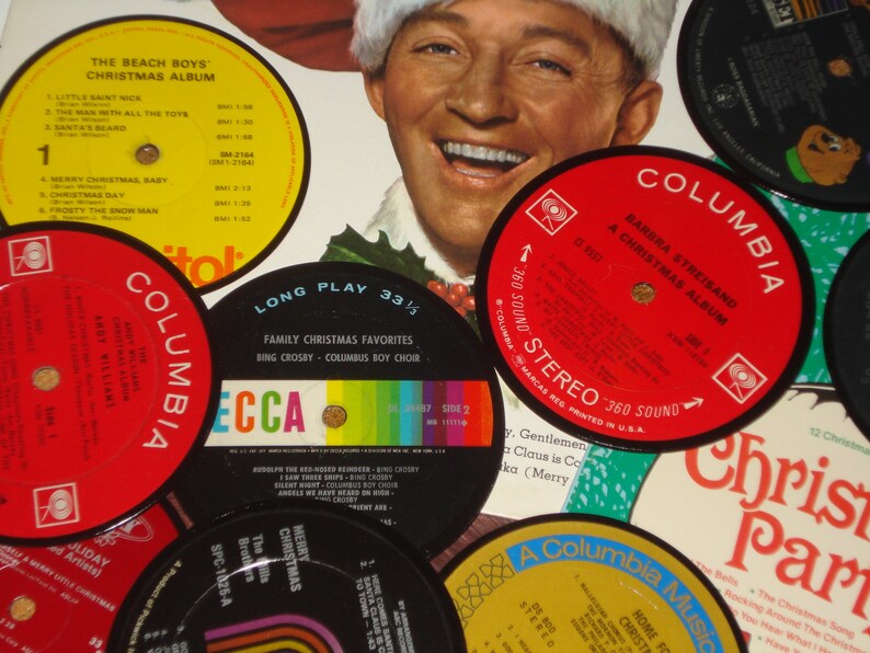 May include: A collection of vintage Christmas vinyl records, including albums by The Beach Boys, Barbra Streisand, and Bing Crosby. The records feature colorful labels with song titles and artist names, creating a festive holiday theme.