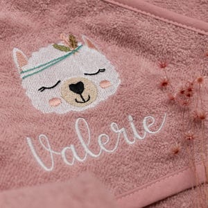 Nahaufnahme der Kapuze von einem altrosafarbenen Handtuch. Als Motiv wurde ein weißes Alpaka mit Federschmuck gestickt. Der Name "Valerie" wurde ebenfalls in weiß in einer hübschen Schreibschrift gestickt.