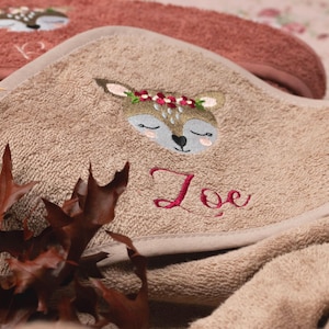 Nahaufnahme der Kapuze von einem rosenholzfarbenen Handtuch. Als Motiv wurde ein Reh mit rotem Blumenstirnband gestickt. Der Name "Zoe" wurde ebenfalls in rot in einer hübschen Schreibschrift gestickt.