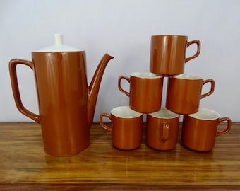 May include: A set of brown ceramic coffee mugs and a matching coffee pot with a white lid. The mugs are stacked in a pyramid shape.