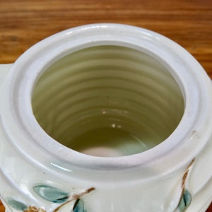 May include: White ceramic teapot with a floral design. The teapot has a wide opening and a handle on the side.