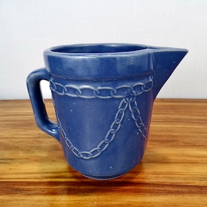 May include: A blue ceramic pitcher with a chain design. The pitcher has a handle and a spout.