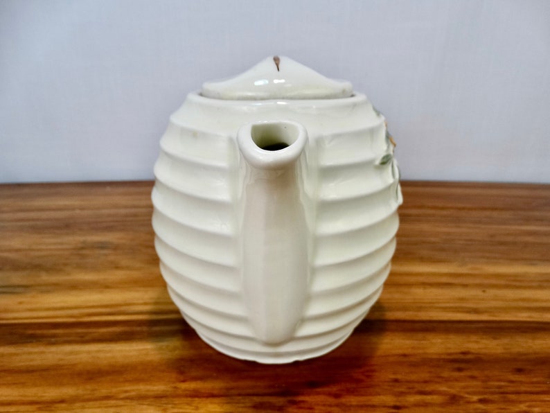 May include: White ceramic teapot with a ribbed design and a floral pattern. The teapot has a spout and a lid.