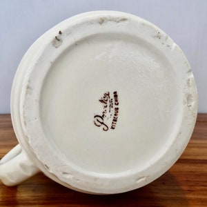 May include: The base of a white ceramic mug with a brown "Porcelite Vitreous China" stamp.