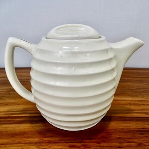 May include: White ceramic teapot with a ribbed design and a lid. The teapot has a rounded body and a spout on one side.
