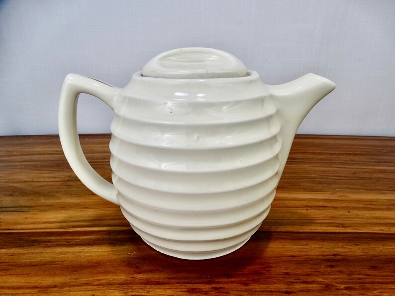 May include: White ceramic teapot with a ribbed design and a lid. The teapot has a rounded body and a spout on one side.