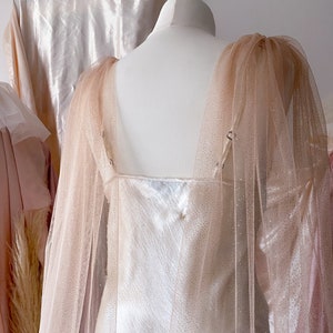Puede incluir: Un vestido blanco con una superposici&oacute;n de tul rosa transparente. El vestido tiene un escote redondo y un corpi&ntilde;o ajustado. La superposici&oacute;n est&aacute; hecha de un tejido de tul delicado con un brillo sutil.