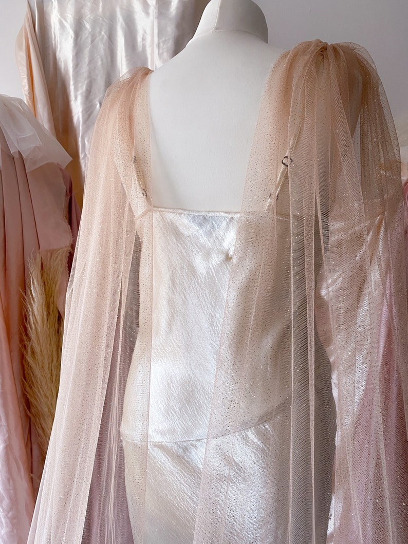 Puede incluir: Un vestido blanco con una superposici&oacute;n de tul rosa transparente. El vestido tiene un escote redondo y un corpi&ntilde;o ajustado. La superposici&oacute;n est&aacute; hecha de un tejido de tul delicado con un brillo sutil.