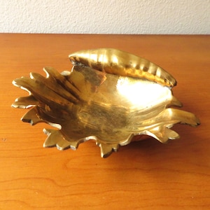 May include: A gold-colored metal dish shaped like a crab with a detailed design. The dish is on a wooden surface.