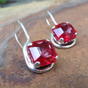 May include: A pair of silver dangle earrings with red square-shaped gemstones.