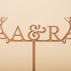 May include: Wooden cake topper with antlers on either side and the letters A & R in the centre.