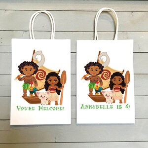 May include: Two white paper gift bags with handles. The bags feature a cartoon image of Moana and Maui from the Disney movie Moana. One bag says "You're Welcome!" and the other says "Annabelle is 6!"