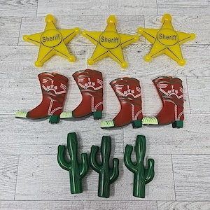 May include: A collection of Western-themed decorative items, including three yellow sheriff stars with the word "Sheriff", four red cowboy boots, and three green cactus figures. The items are arranged on a light wood-grain surface.