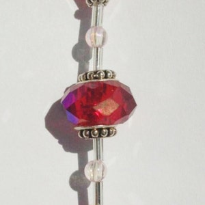 Puede incluir: Un atrapasol de cristal con un cristal en forma de lágrima y cuentas de vidrio rojas. Las cuentas están enhebradas en un alambre de plata.