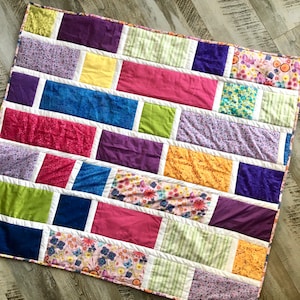 May include: A colorful patchwork quilt with a variety of floral and geometric patterns in shades of pink, purple, yellow, blue, and green.