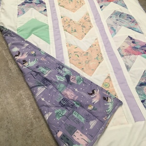 May include: A white, purple, and green chevron patterned quilt with a purple and green floral pattern on the back.