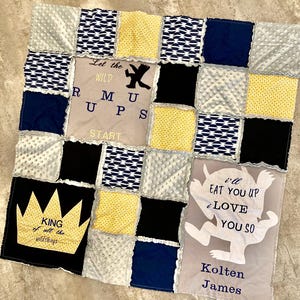 Puede incluir: Una manta de bebé patchwork con cuadrados de tela en azul marino, negro, amarillo y gris. Algunos cuadrados tienen patrones, otros son lisos. El texto incluye "Let the Wild Rumps Start" y "King of all the wild things."