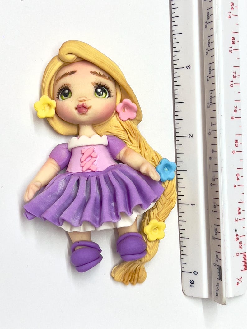 May include: A handcrafted polymer clay figurine of a princess with long blonde hair, green eyes, and a purple dress. The figurine is adorned with yellow, pink, and blue flower accents. The figure is approximately 3 inches tall.